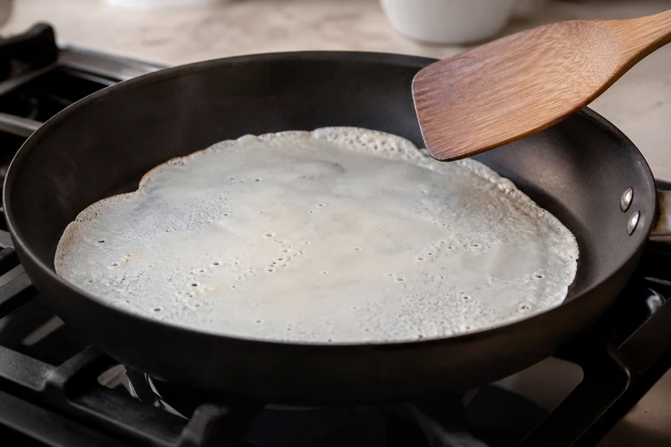 Thin blini batter spreading and setting in an unbranded skillet.