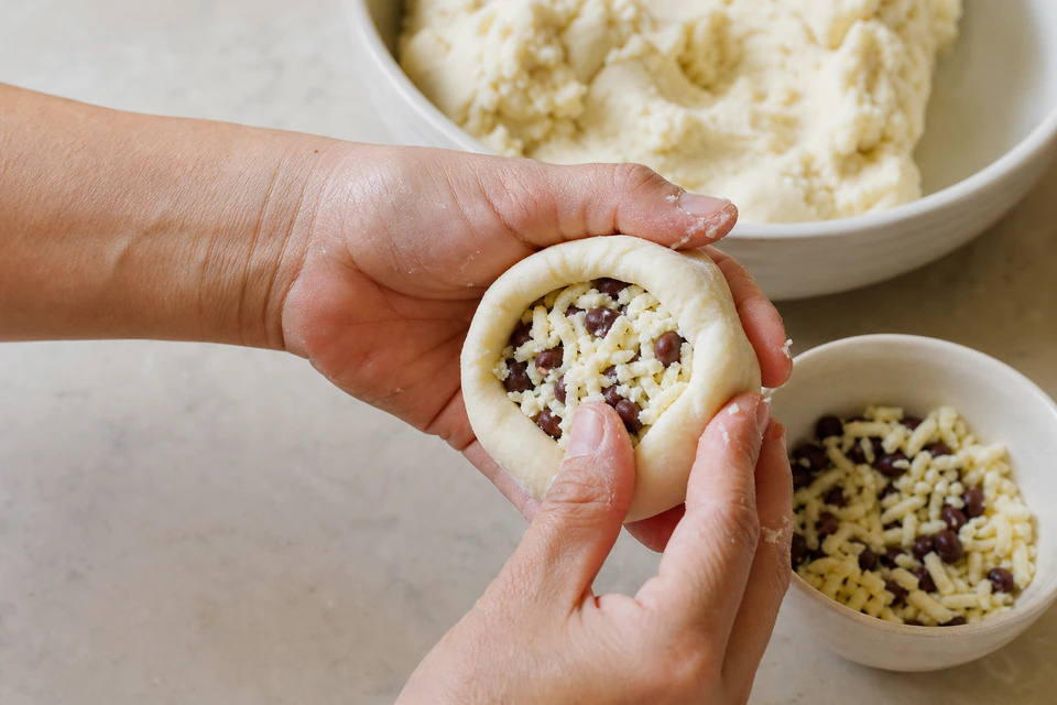 Hands closing masa around a bean and cheese filling while shaping a pupusa.