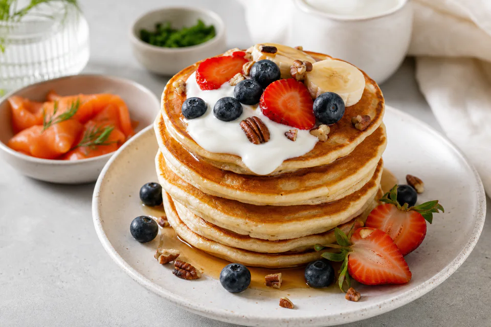 Finished pancake stack with berries, banana, yogurt, pecans, and a restrained syrup drizzle