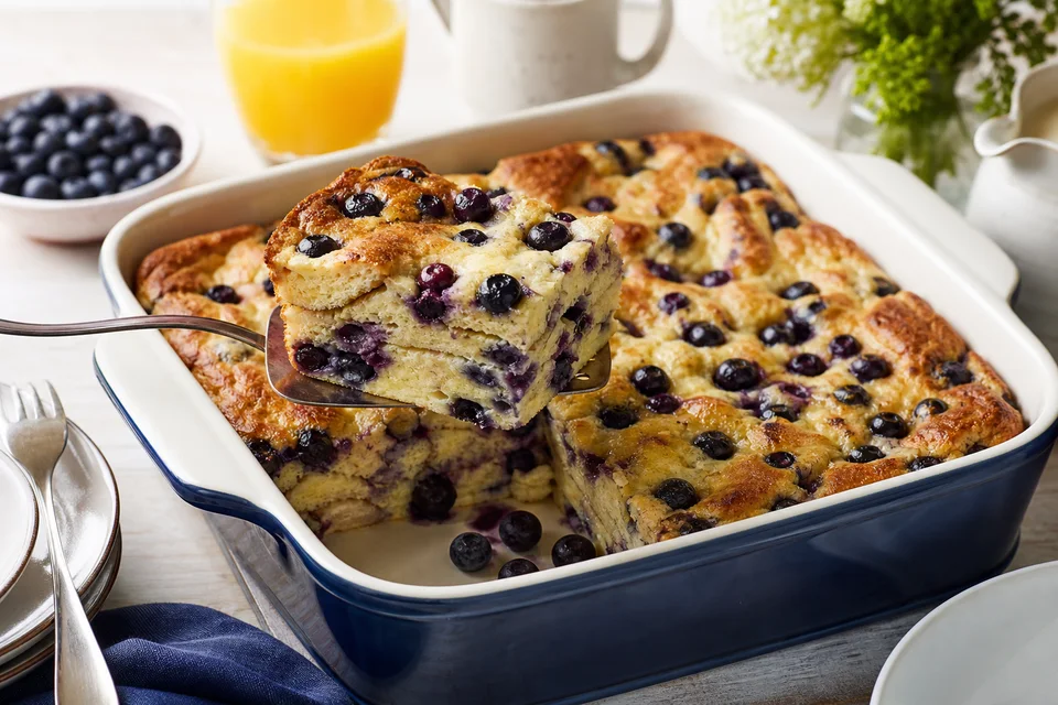 A browned blueberry pancake breakfast casserole with one square lifted to show berries and pancake layers.