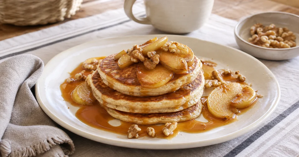 Golden pancakes with amber caramel, sauteed apple slices, and toasted walnuts on a finished breakfast plate.
