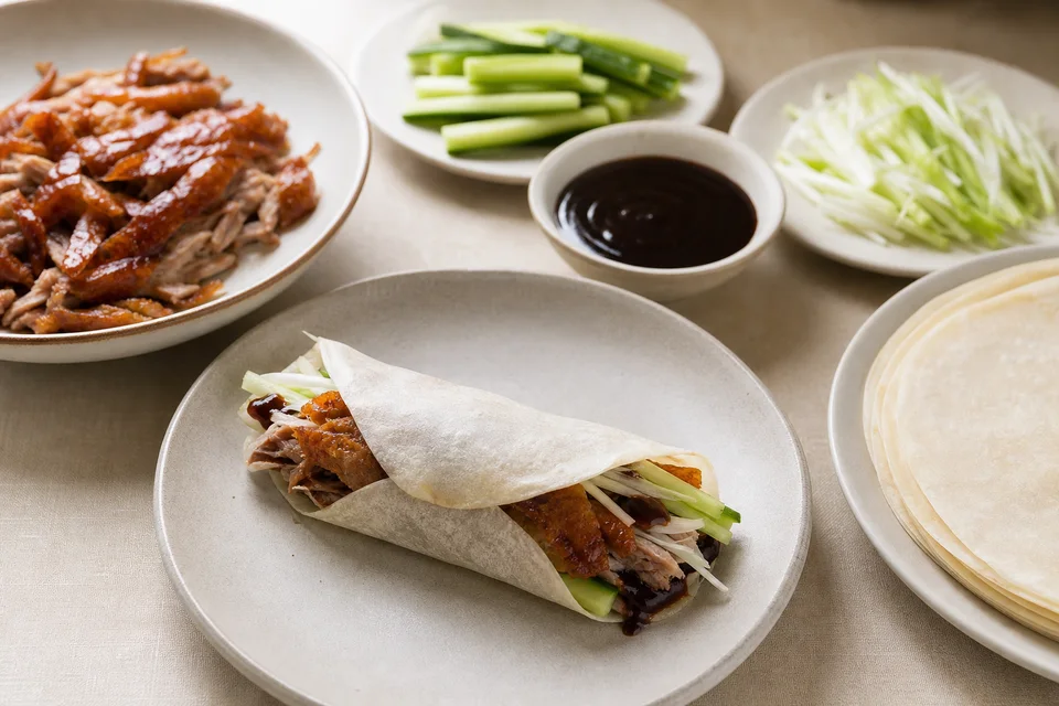 Thin wrappers, crisp cooked duck, cucumber, scallions, and sauce arranged around one rolled duck pancake.