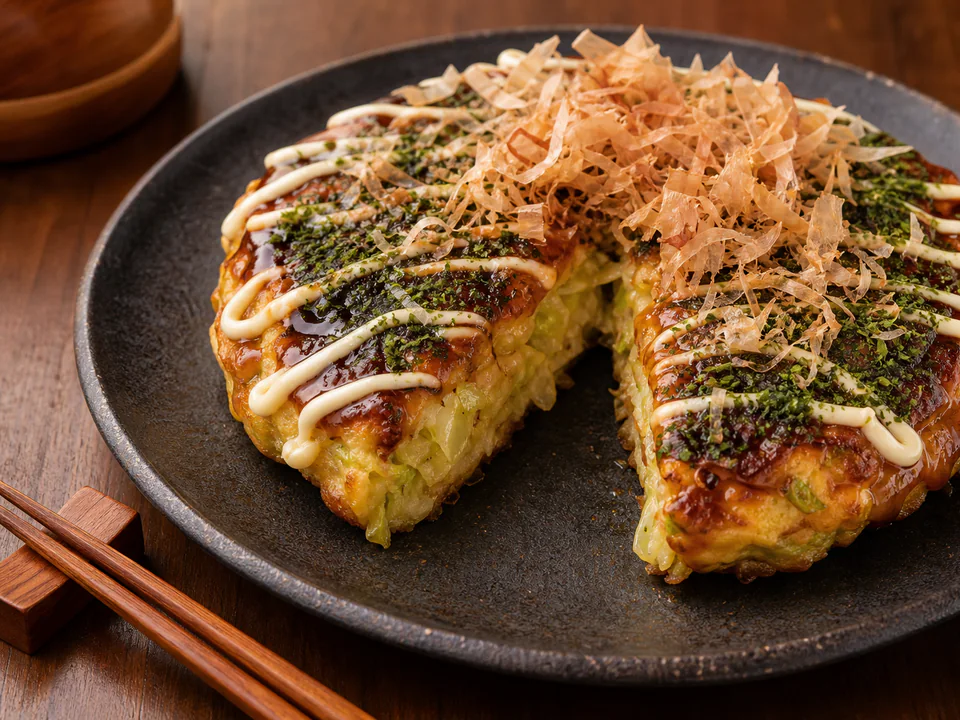 Close detail of the cabbage-rich okonomiyaki interior beneath sauce, mayonnaise, and bonito