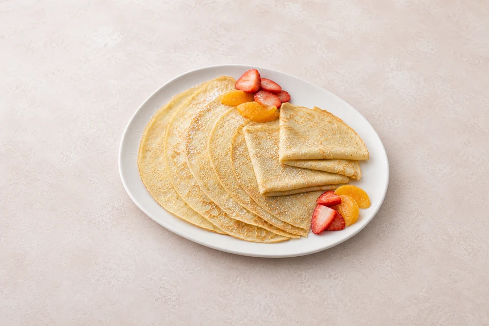 Finished thin golden pancakes folded into quarters with fresh fruit