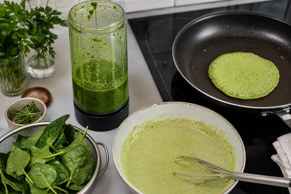 Spinach and herbs blended into green pancake batter beside one small test pancake cooking.