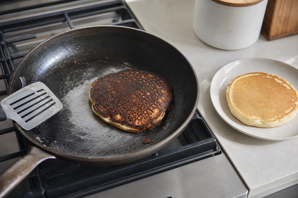An over-browned pancake in a real skillet beside a pale control pancake used to reset the cooking heat.