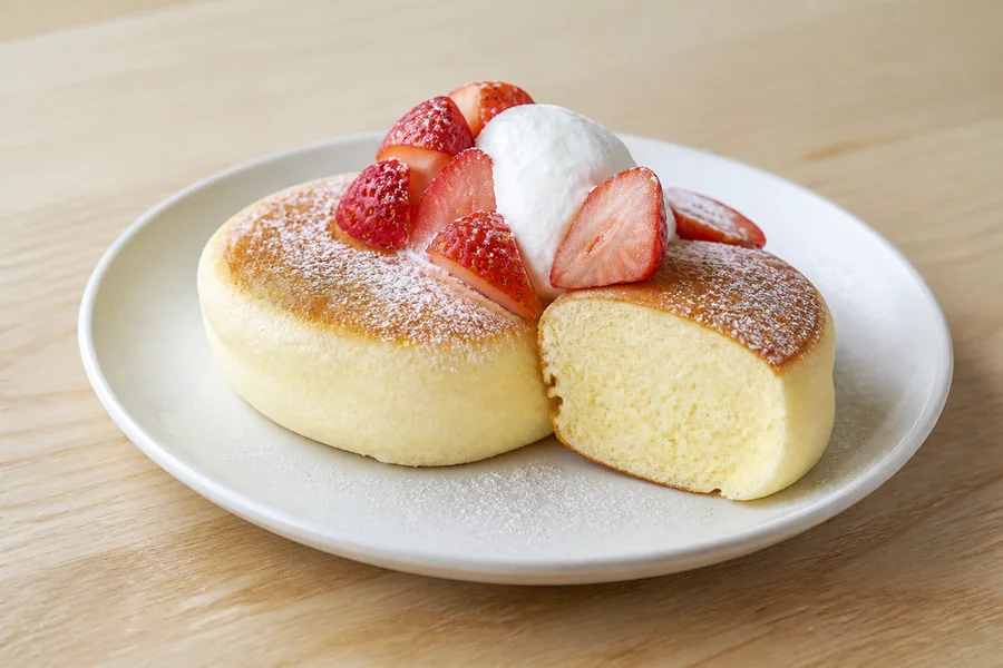 Close detail of tall Japanese soufflé pancakes with a cooked airy crumb, strawberries, and cream.