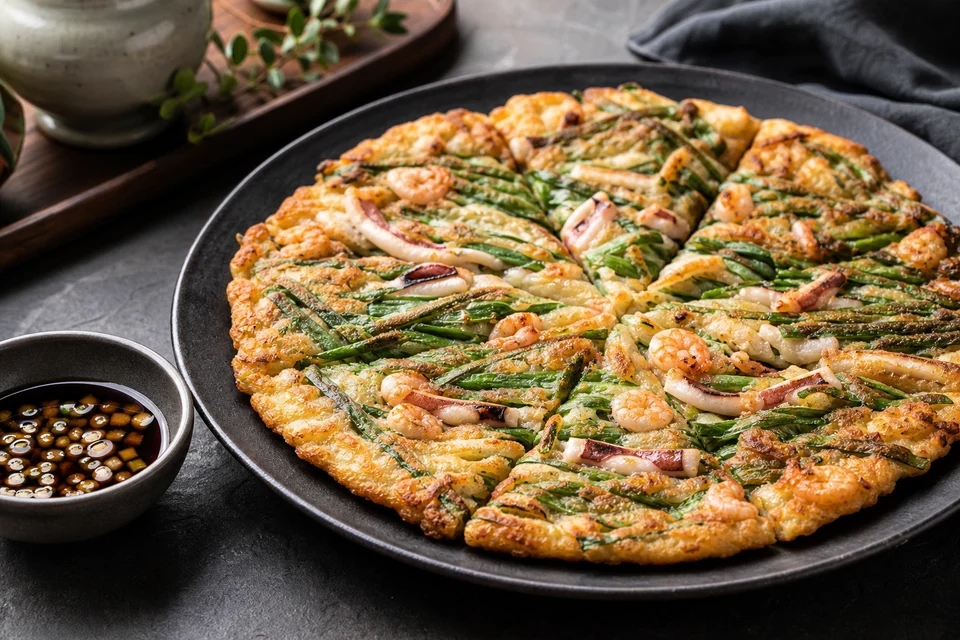 Crisp Korean seafood pajeon cut into wedges with scallions, shrimp, squid, and soy dipping sauce.