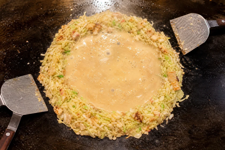 Monjayaki ingredients arranged in a ring around thin batter on a hot griddle.