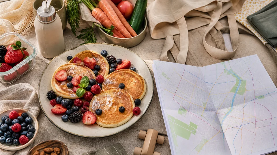 Pancake picnic with berries beside a folded transit map, reusable bottle, tote and vegetables.