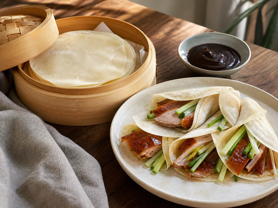 Close detail of thin wrappers folded around cooked duck, cucumber, and scallion