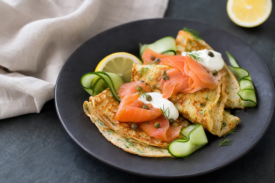 Thin herb pancakes with ready-to-eat smoked salmon, crème fraîche, capers, dill, cucumber, and lemon.