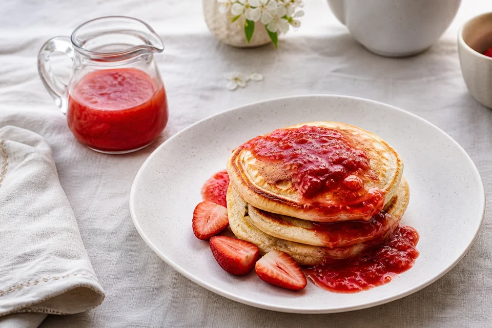 Homemade strawberry syrup with natural fruit texture served over a finished stack of golden pancakes.