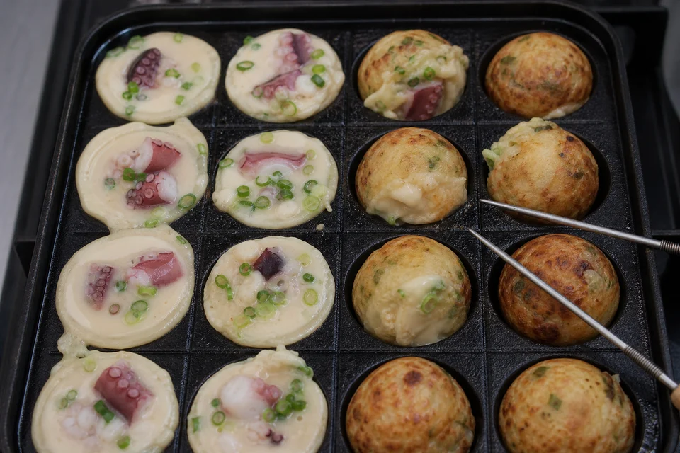 Takoyaki batter and octopus setting in a dimpled pan during the first staged turn.