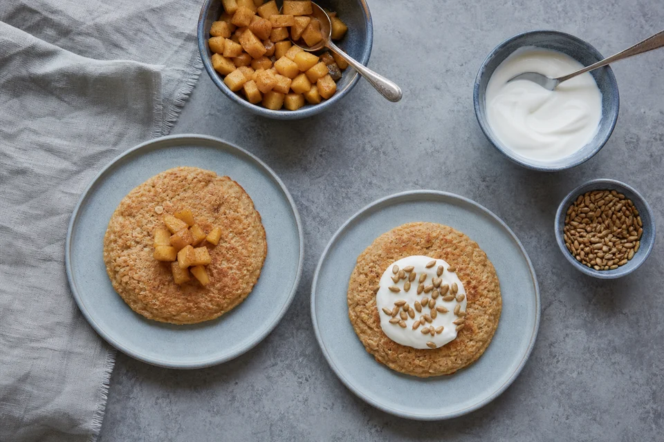 Two finished oatmeal pancakes used to compare a warm apple topping with a yogurt and seed topping.