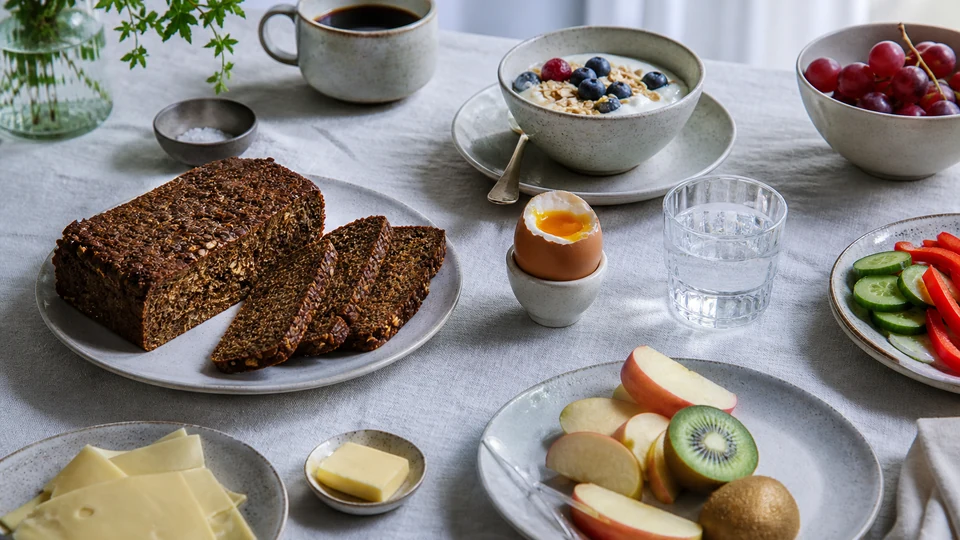 Danish breakfast table with rye bread, cheese, soft-boiled egg, yogurt, and pastries.